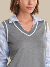 Woman wearing a gray sweater vest over a striped shirt against a neutral background