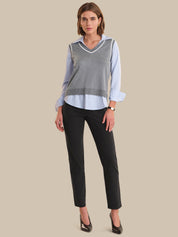 Woman wearing a gray sweater vest over a striped shirt with black pants on a beige background