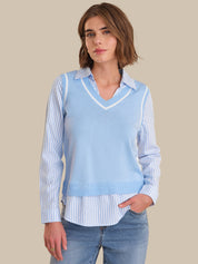 Woman wearing a light blue sweater vest over a striped shirt with jeans on a beige background