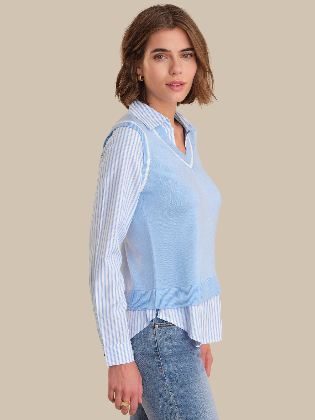 Woman wearing a light blue sheer top over a striped shirt with jeans on a beige background
