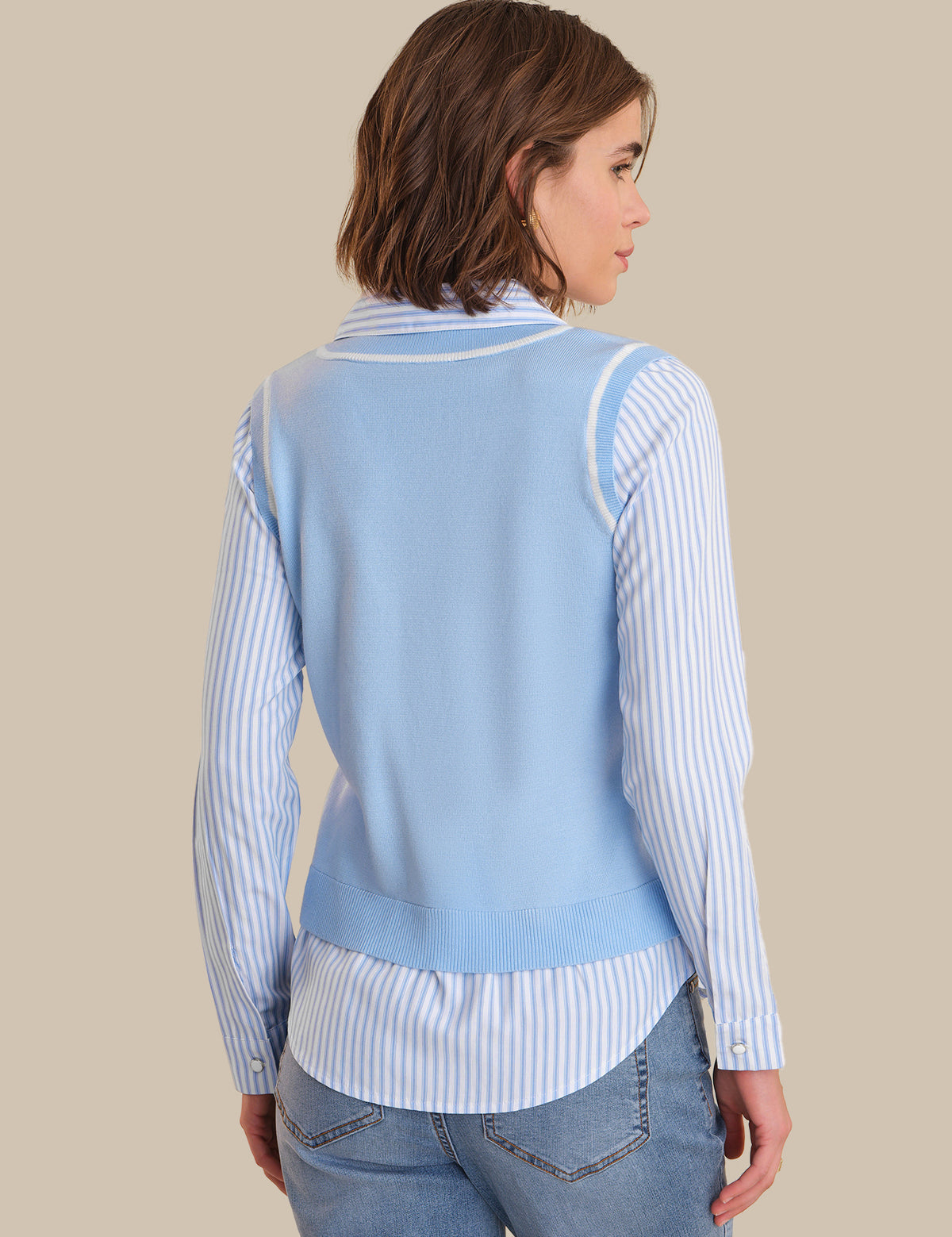 Woman wearing a light blue sweater over a striped shirt with a beige background