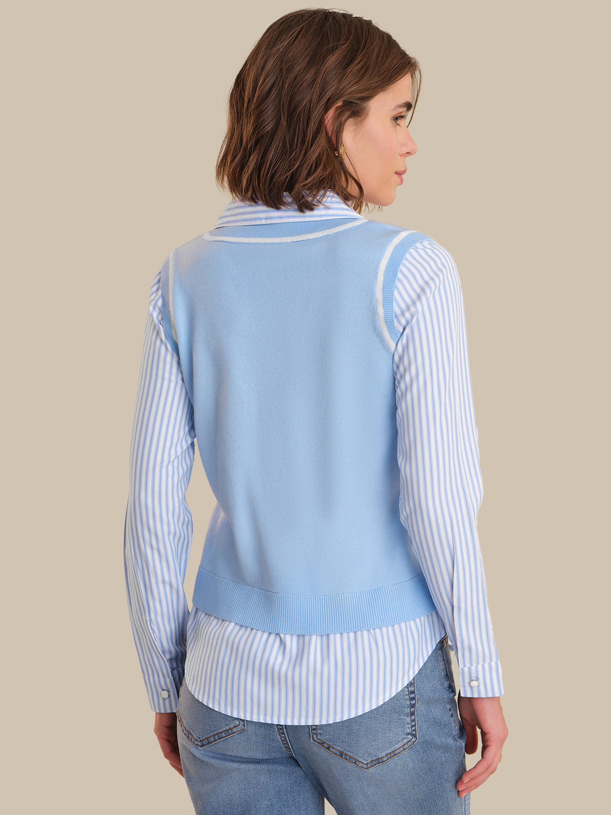 Woman wearing a light blue sweater over a striped shirt with a beige background