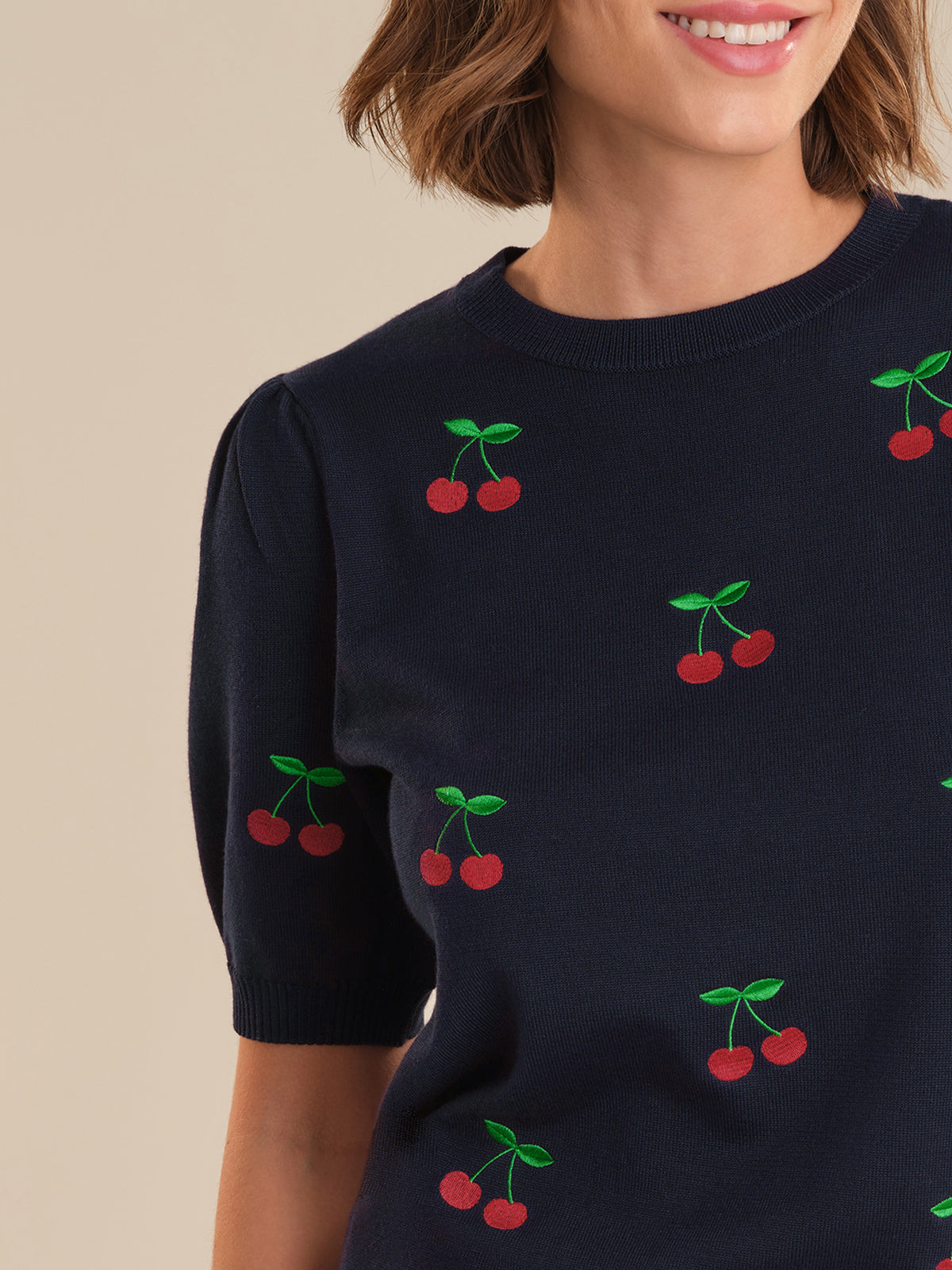 Navy sweater with cherry pattern worn by a person on a beige background