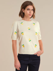 Woman wearing a cream-colored top with lemon designs on a beige background