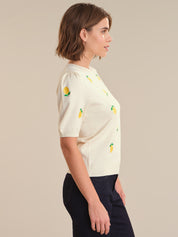 Woman wearing a cream-colored blouse with pineapple patterns on a beige background