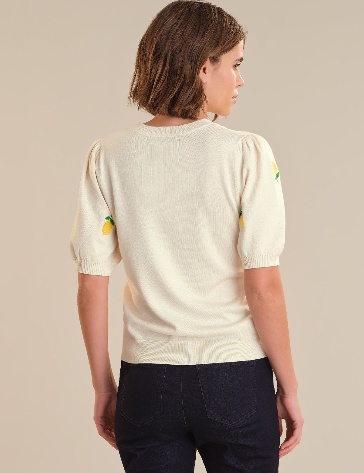 Person wearing a cream-colored sweater with colorful accents on a beige background