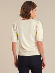 Person wearing a cream-colored sweater with colorful accents on a beige background