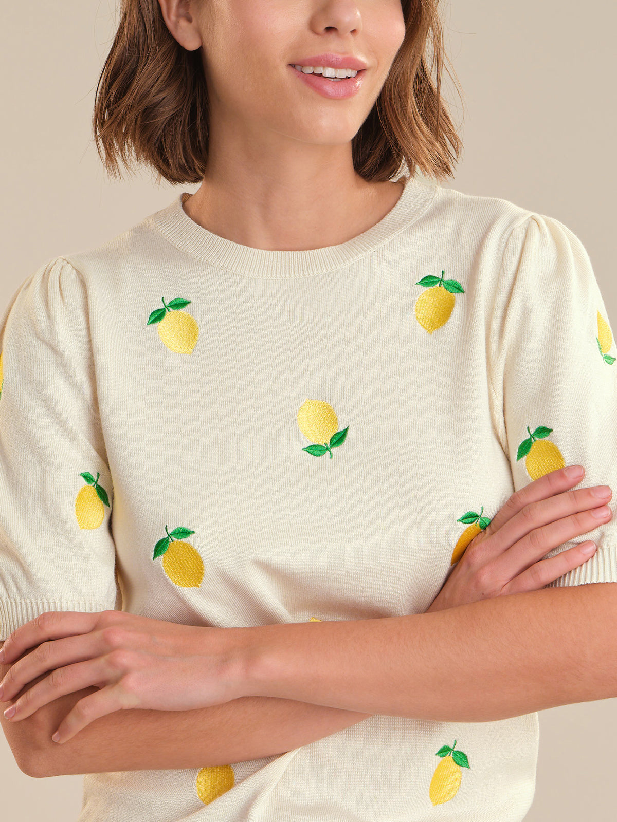 Woman wearing a cream sweater with lemon designs on a beige background