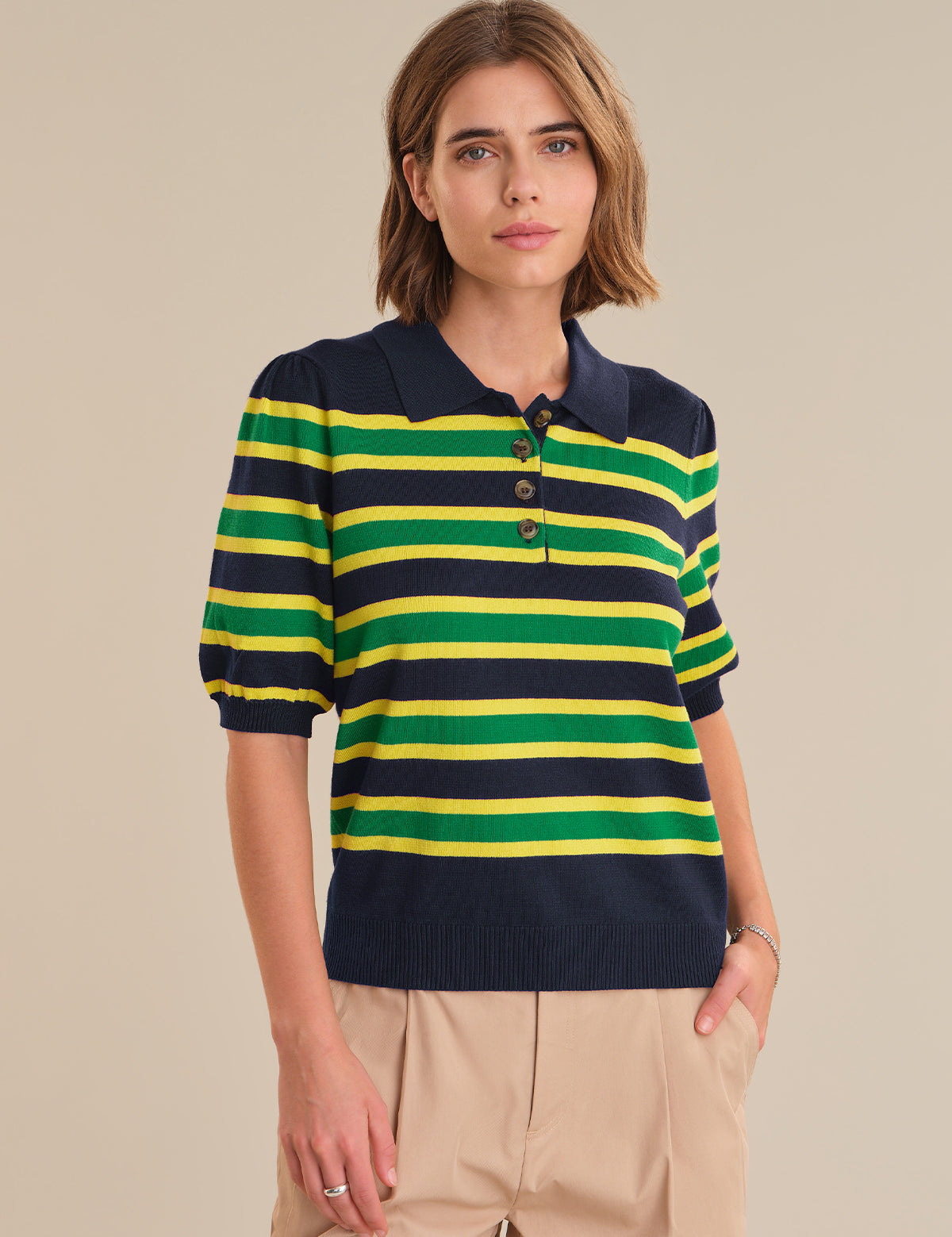 Woman wearing a striped polo shirt with navy, green, and yellow colors on a beige background