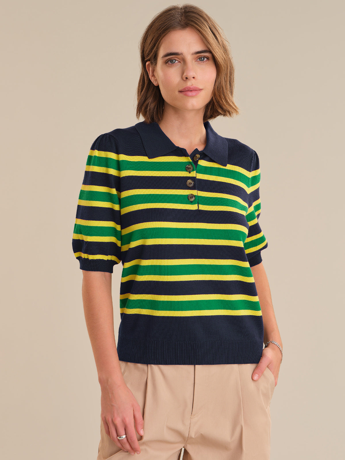 Woman wearing a striped polo shirt with navy, green, and yellow colors on a beige background