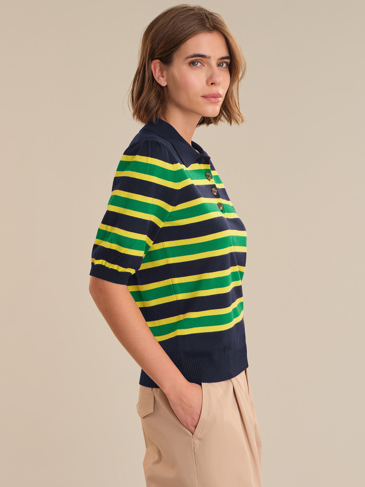 Woman wearing a navy and green striped polo shirt against a beige background