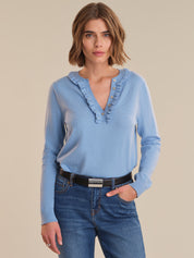 Woman wearing a light blue sweater with ruffled details and blue jeans on a beige background