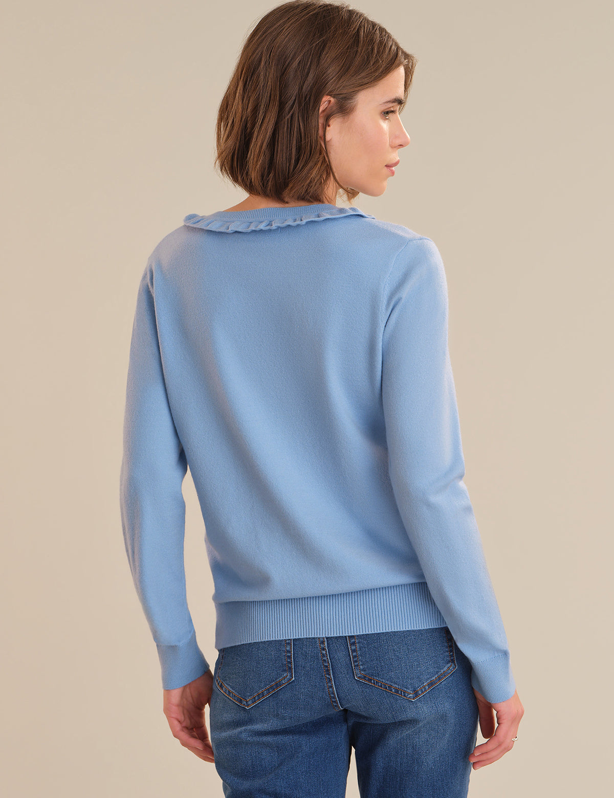 Woman wearing a light blue sweater with a textured collar against a beige background