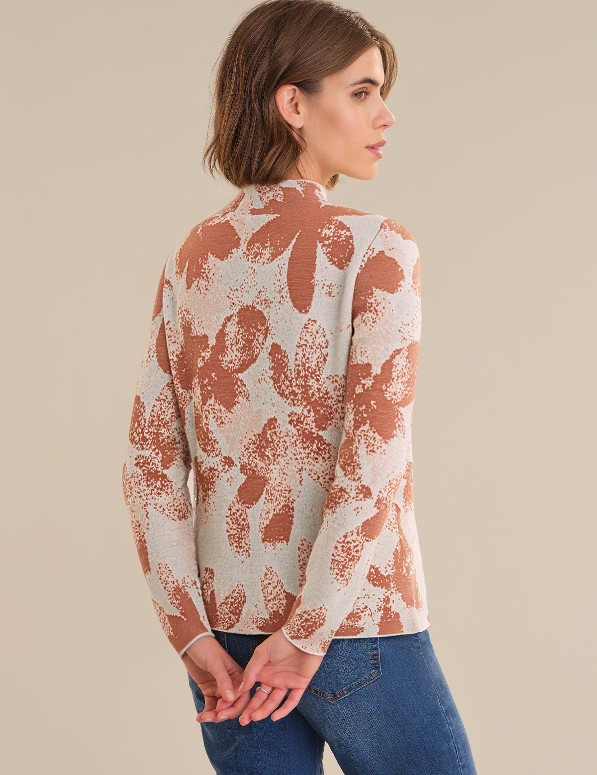 Woman wearing a patterned long-sleeve top and blue jeans on a beige background