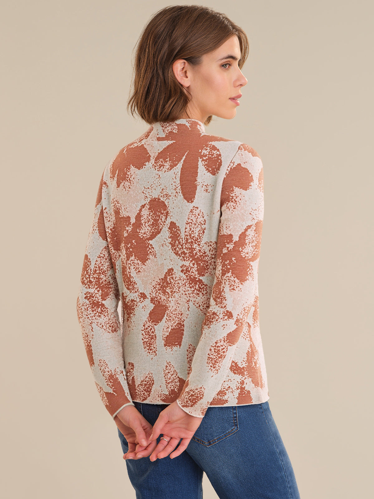 Woman wearing a patterned long-sleeve top and blue jeans on a beige background