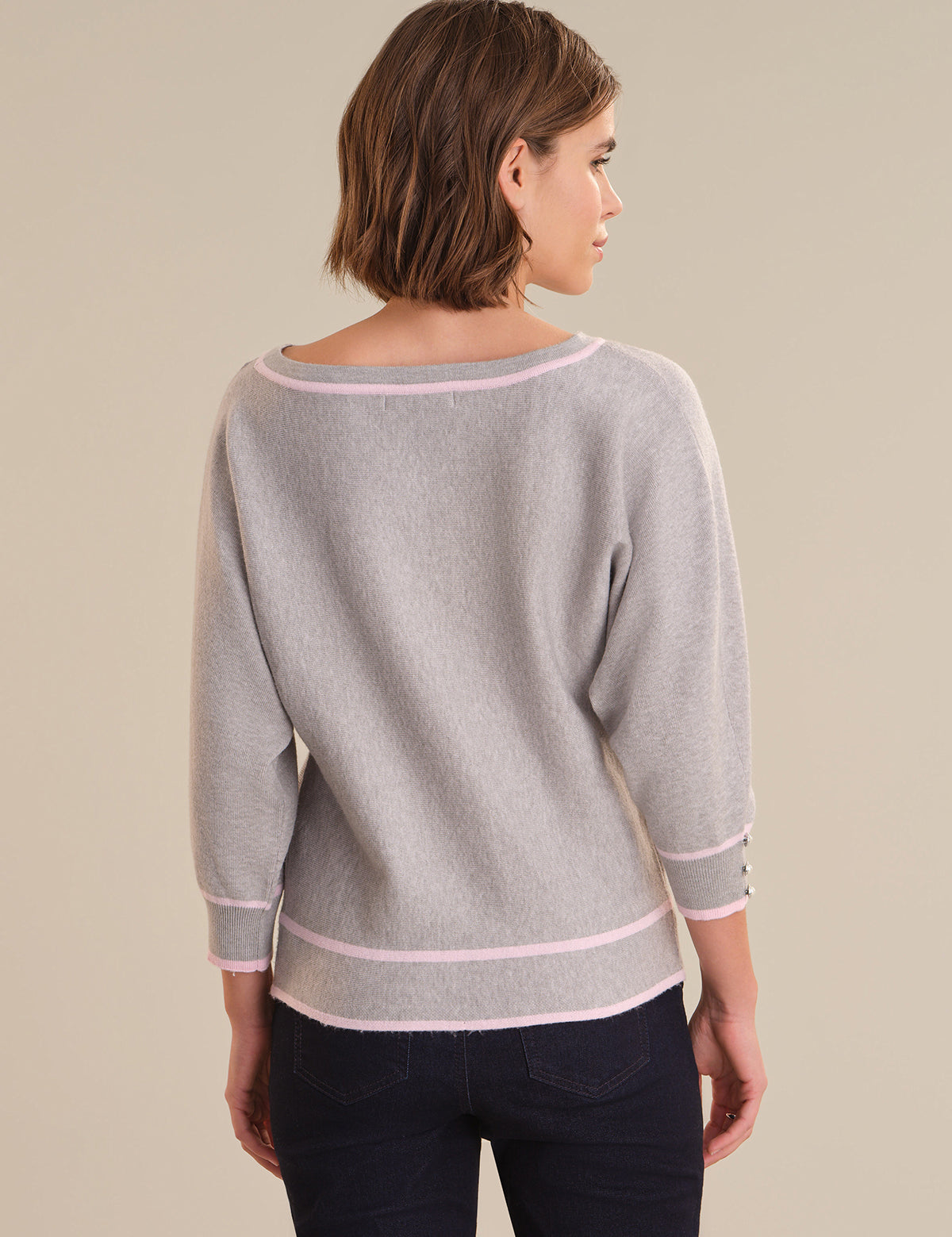 Woman wearing a gray sweater with pink trim on a beige background