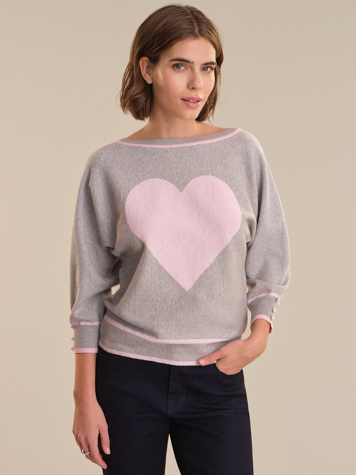 Woman wearing a gray sweater with a pink heart design on a beige background