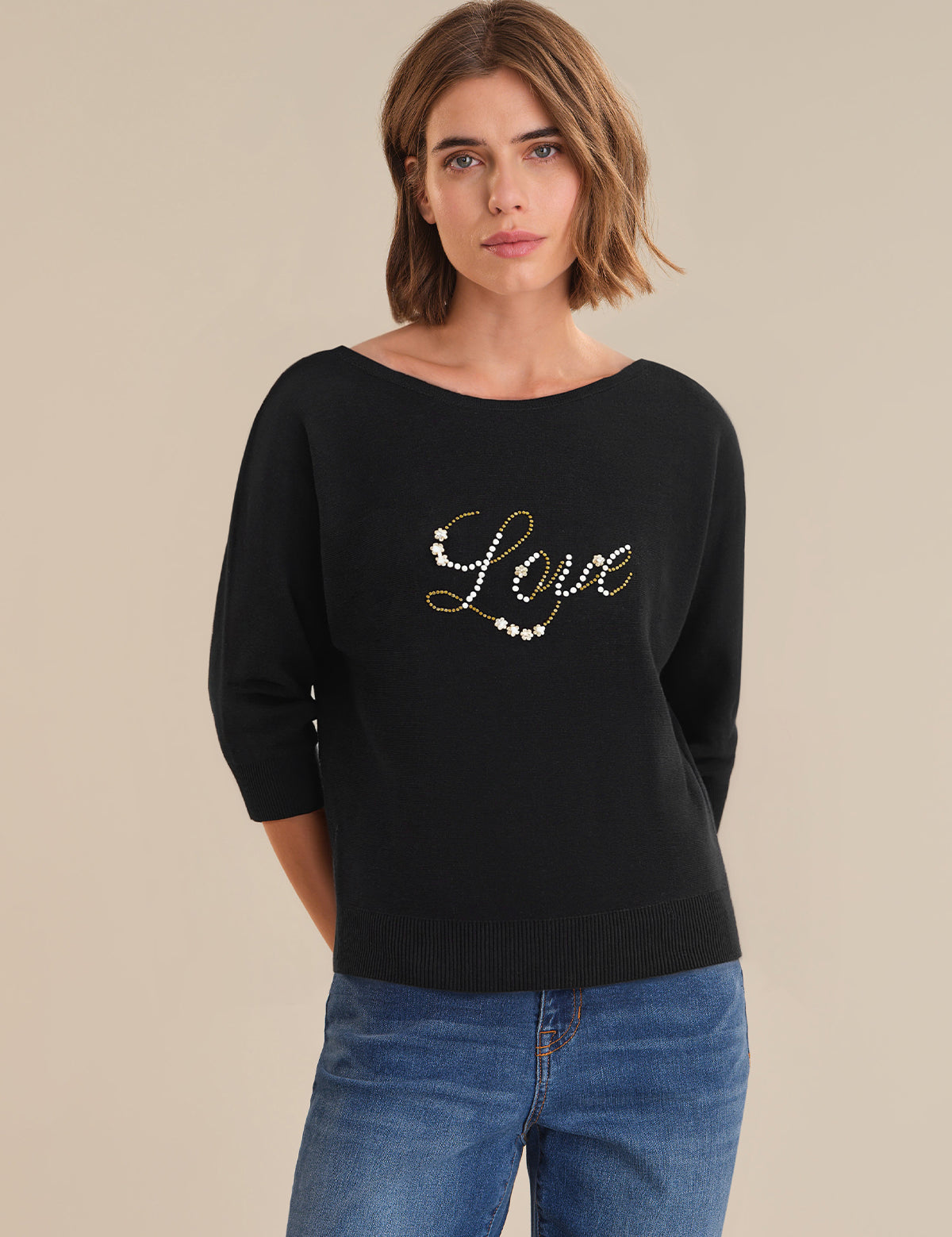 Woman wearing a black sweater with 'Love' embellishments on a beige background