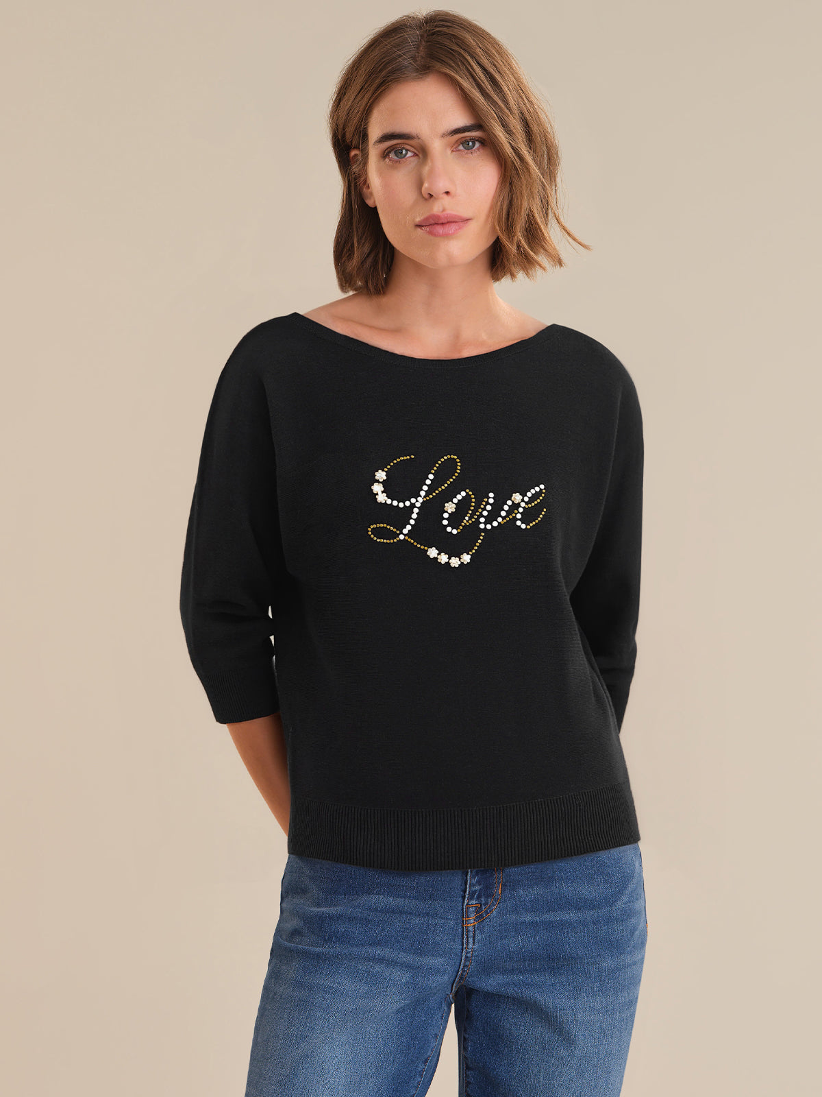 Woman wearing a black sweater with 'Love' embellishments on a beige background