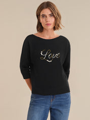 Woman wearing a black sweater with 'Love' embellishments on a beige background