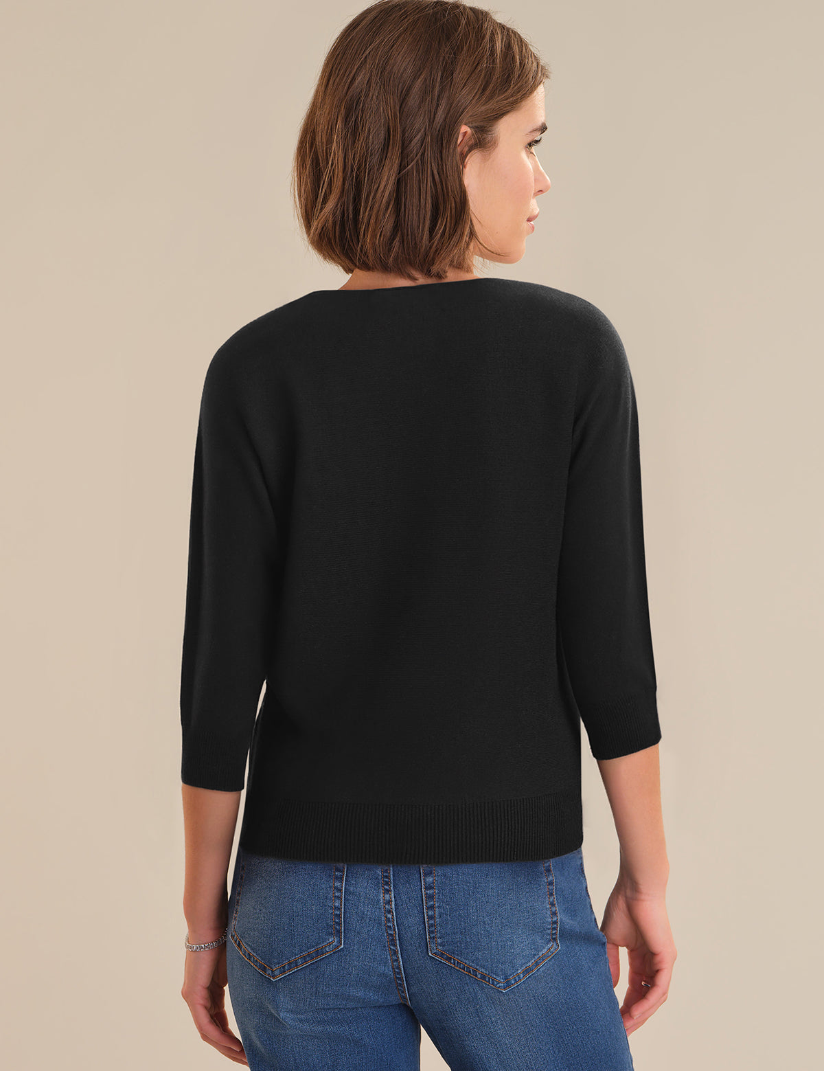 Woman wearing a black sweater and blue jeans on a beige background