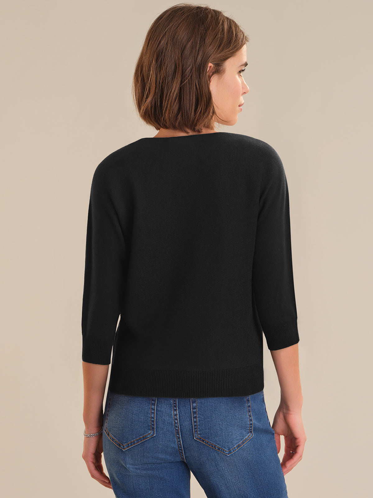 Woman wearing a black sweater and blue jeans on a beige background
