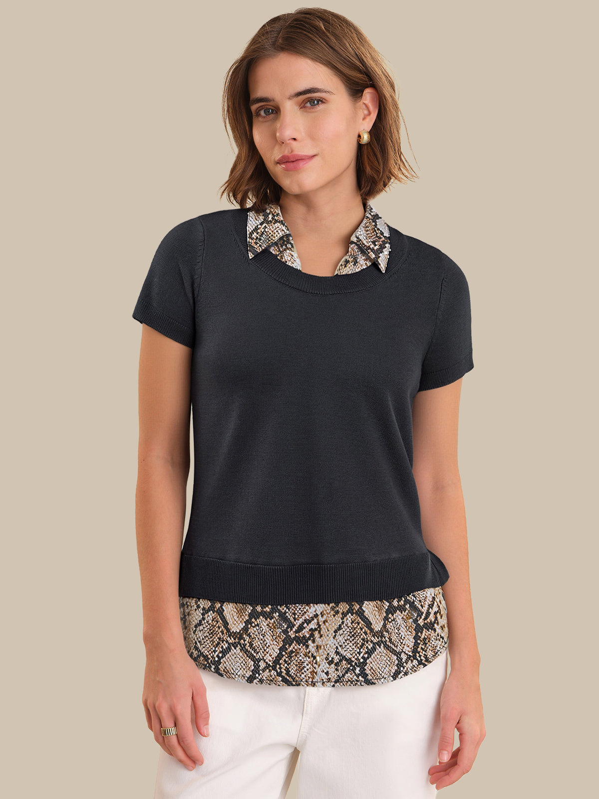 Woman wearing a black top with patterned collar and snake print hem on a beige background