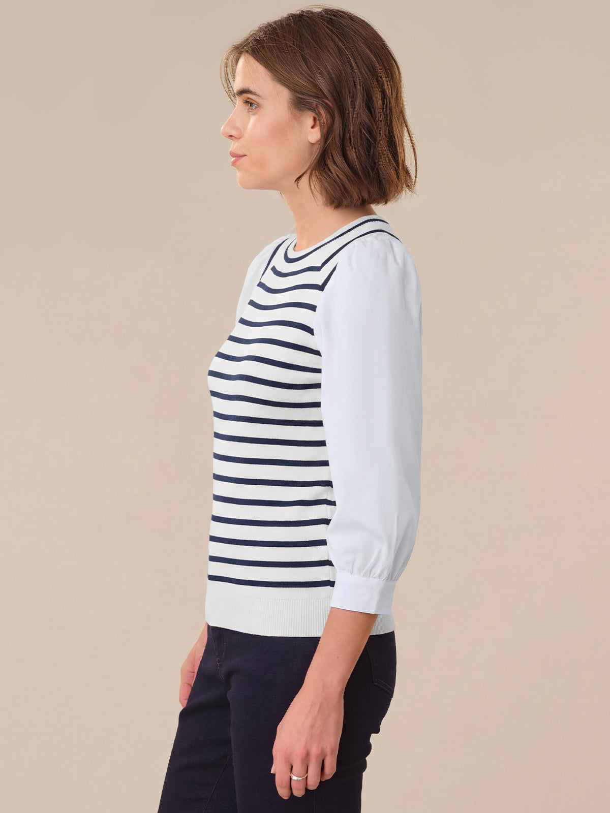 Woman wearing a white sweater with navy stripes against a beige background