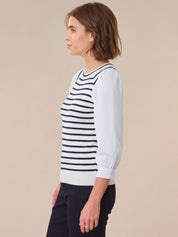 Woman wearing a white sweater with navy stripes against a beige background
