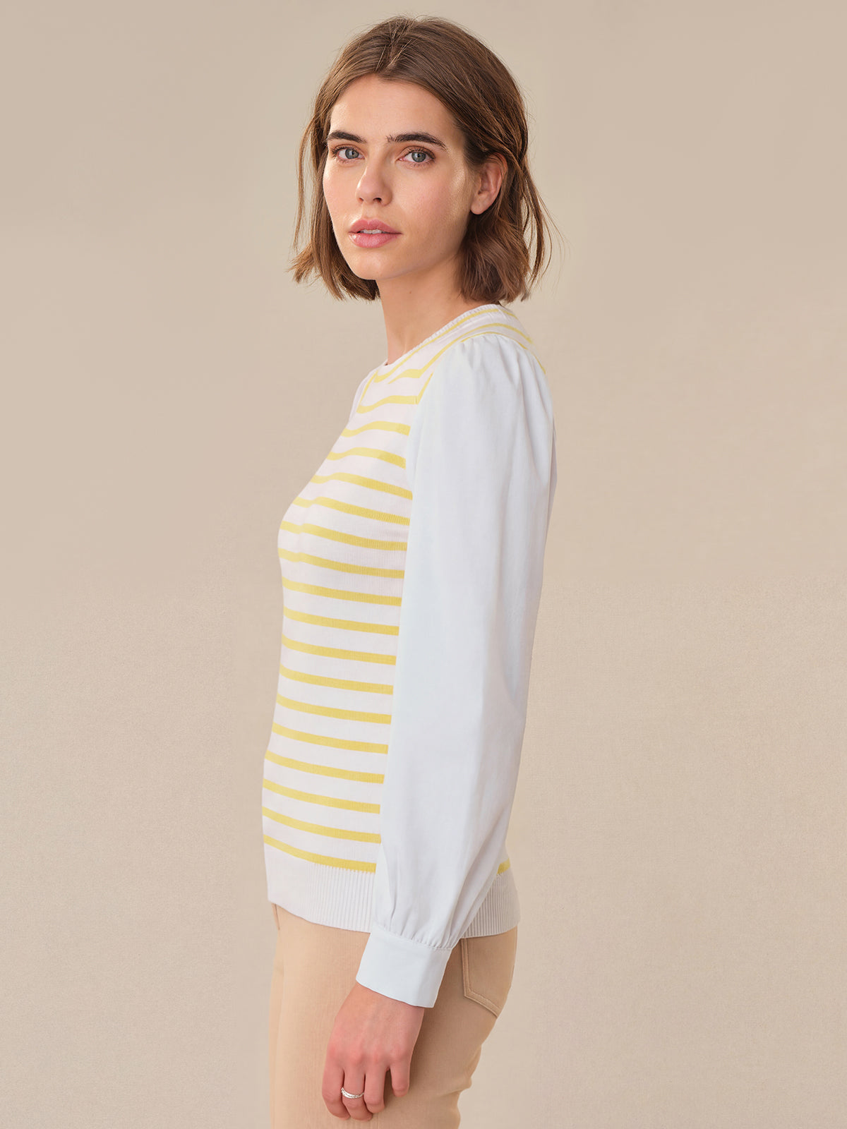 Woman wearing a white long-sleeve shirt with yellow stripes against a beige background