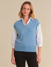 Woman wearing a light blue sweater vest over a white shirt on a beige background