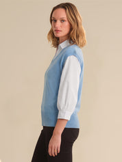 Woman wearing a light blue sweater vest over a white shirt on a beige background