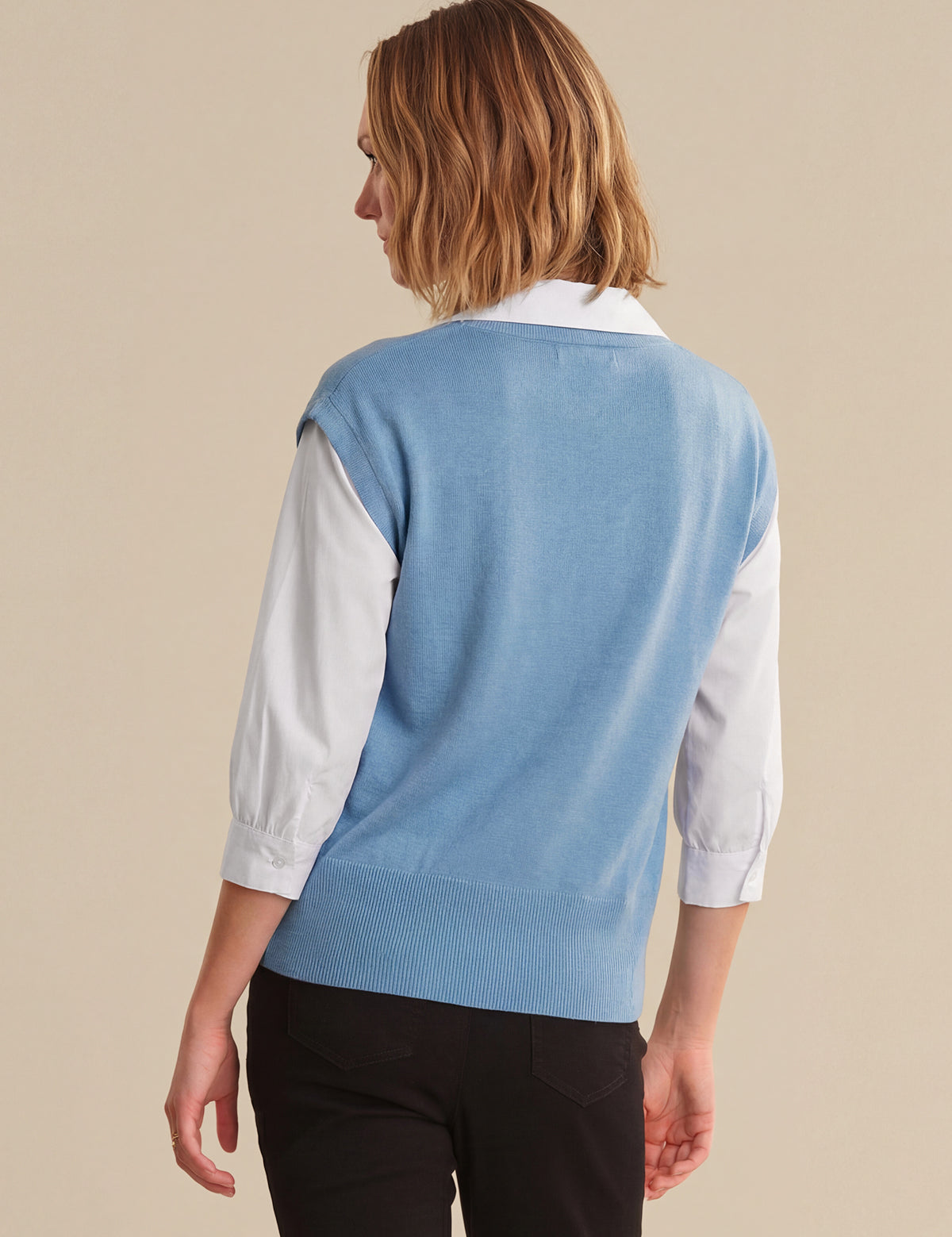 Person wearing a light blue sweater over a white shirt on a beige background
