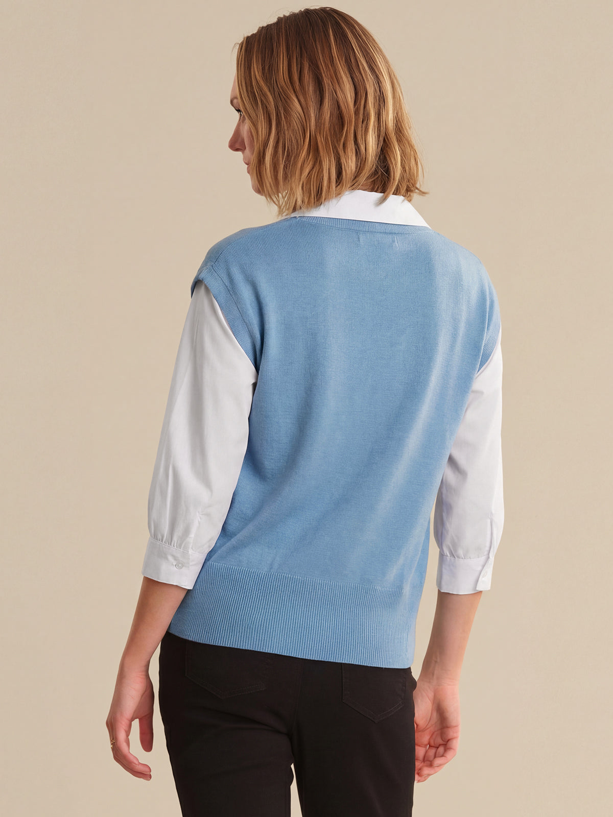 Person wearing a light blue sweater over a white shirt on a beige background