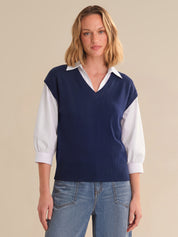 Woman wearing a navy sweater over a white shirt with blue jeans on a beige background