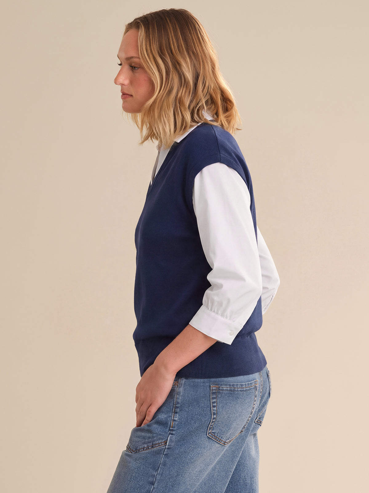 Woman wearing a navy sweater with white sleeves and blue jeans on a beige background