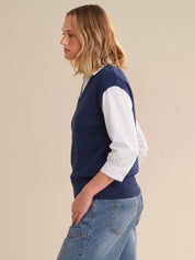 Woman wearing a navy sweater with white sleeves and blue jeans on a beige background