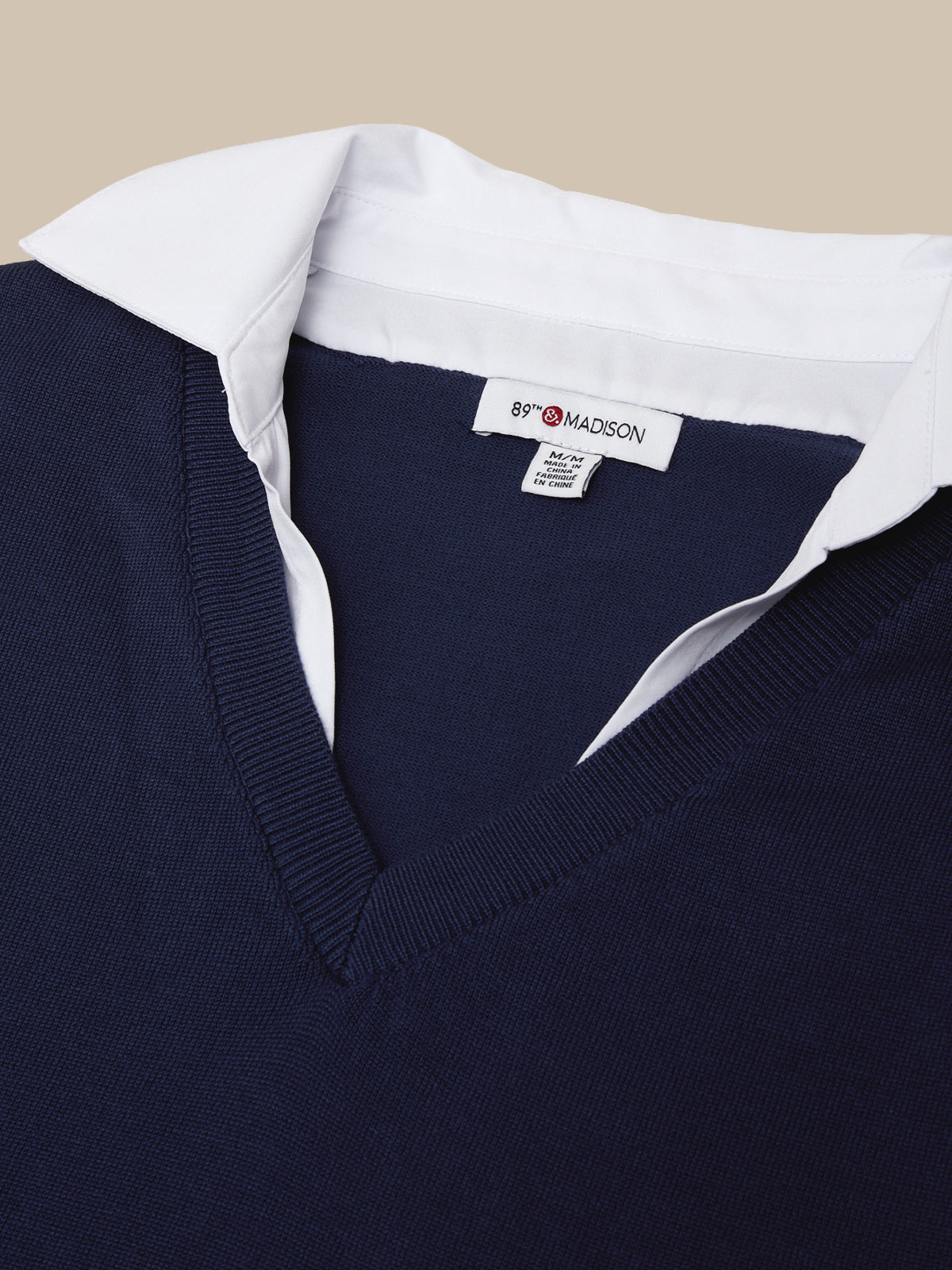Navy sweater with white collar and visible brand label on a beige background