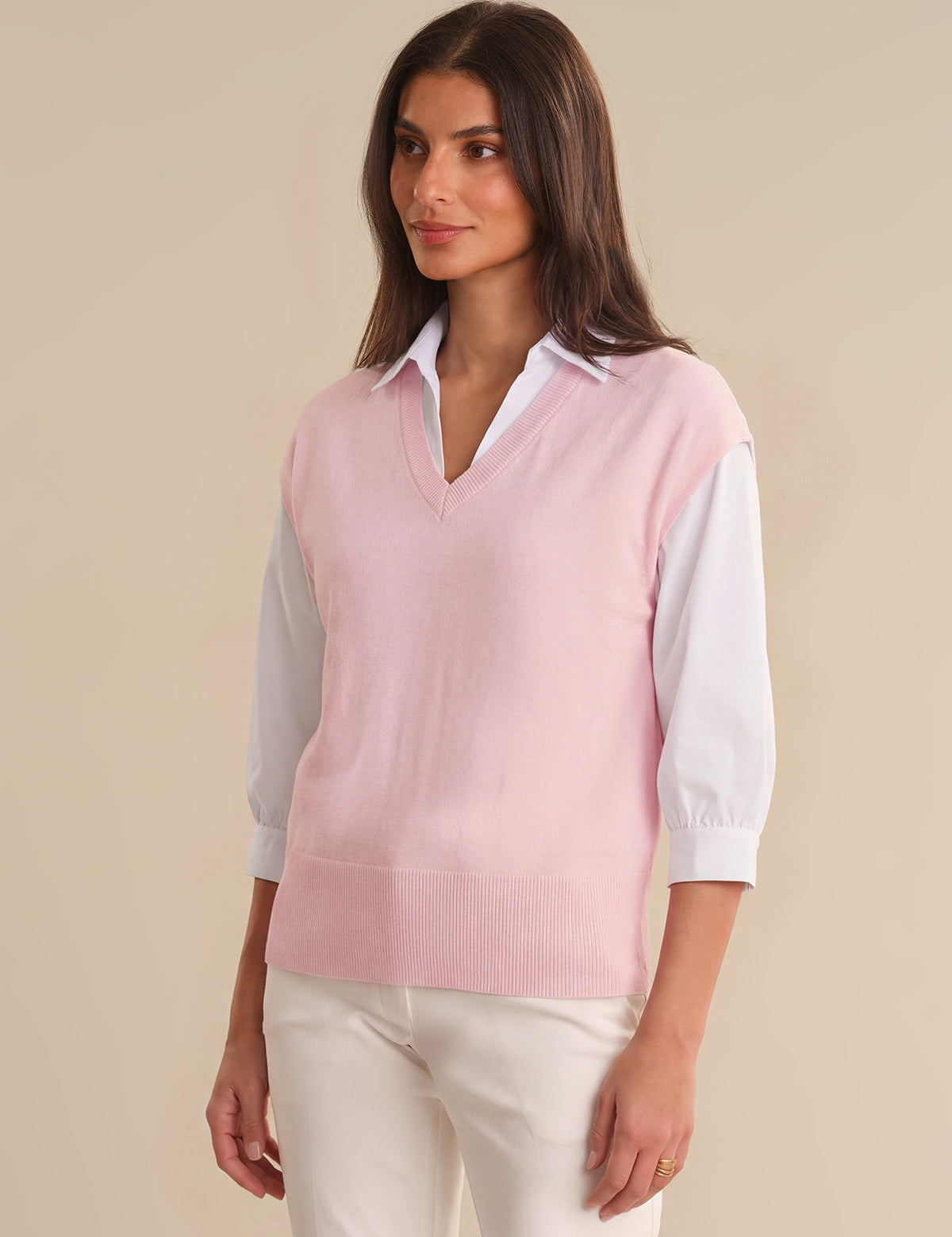 Woman wearing a pink sweater vest over a white shirt on a beige background