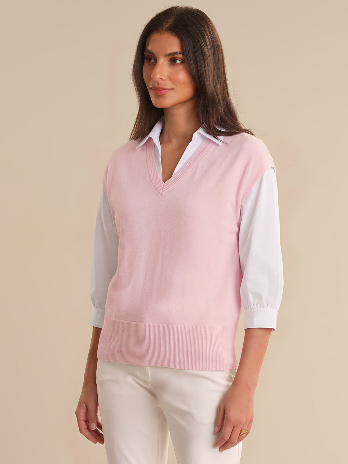 Woman wearing a pink sweater vest over a white shirt on a beige background