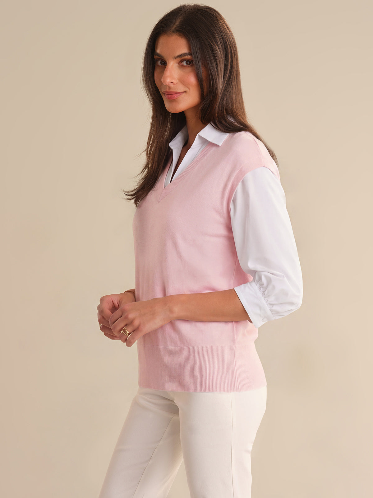 Woman wearing a light pink sweater over a white shirt with beige pants on a beige background
