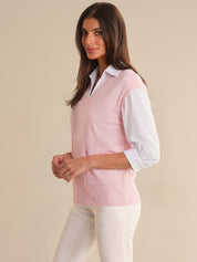 Woman wearing a light pink sweater over a white shirt with beige pants on a beige background