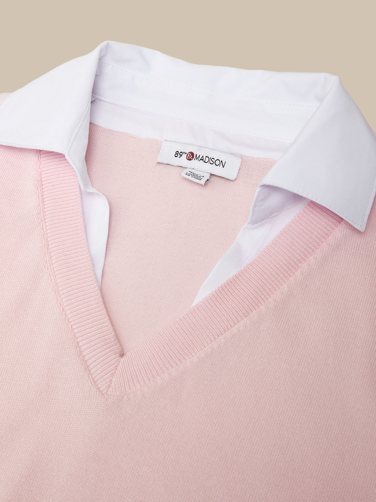 Pink sweater with a white shirt collar and 'Madison' label on a beige background