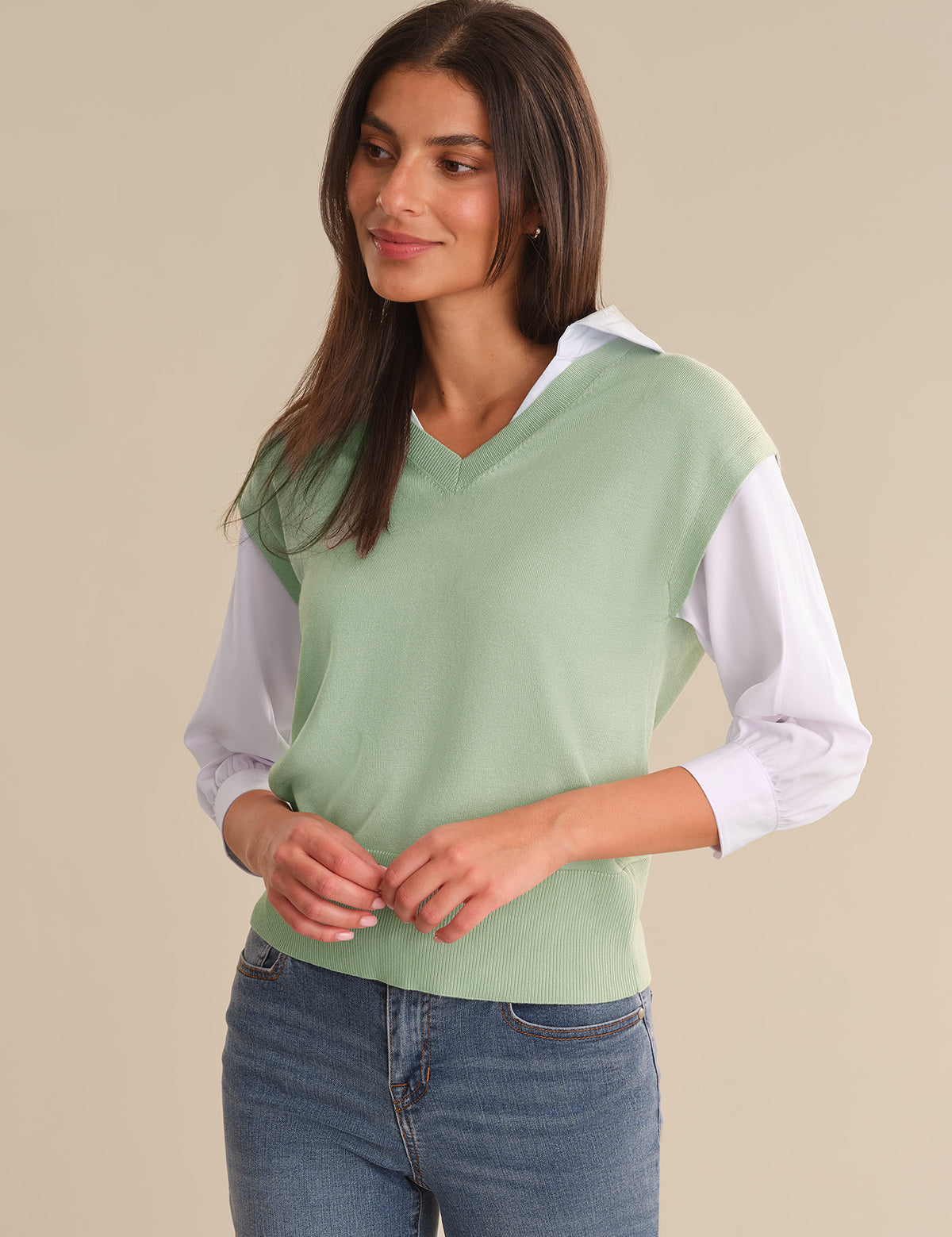 Woman wearing a light green sweater with white sleeves against a beige background