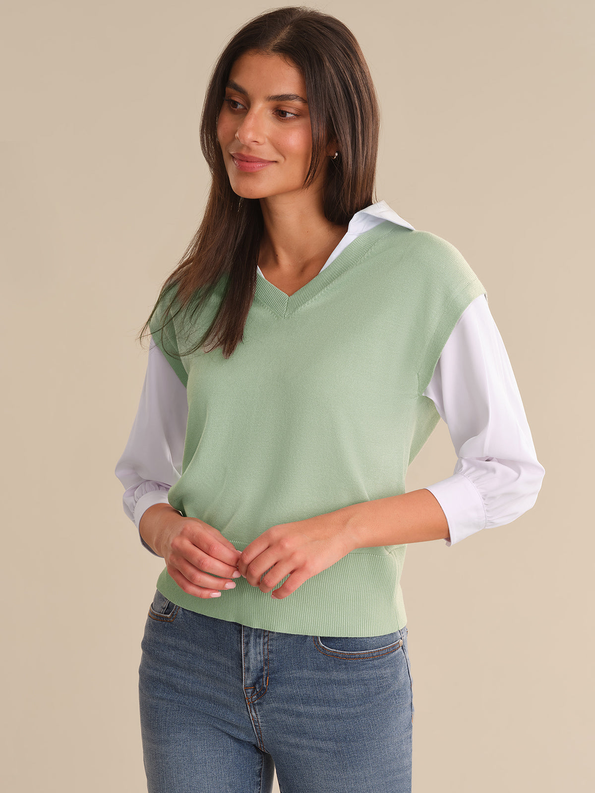 Woman wearing a light green sweater with white sleeves against a beige background