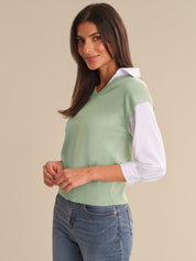 Woman wearing a light green sweater over a white shirt with blue jeans on a beige background