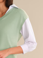 Person wearing a light green sweater over a white shirt on a beige background