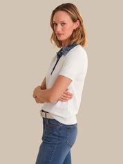 Woman wearing a white shirt with a blue collar and blue jeans against a beige background