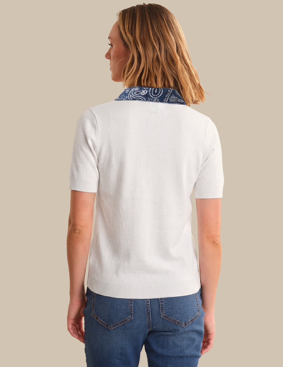 Person wearing a white polo shirt with a blue patterned collar and blue jeans on a beige background
