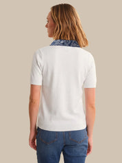 Person wearing a white polo shirt with a blue patterned collar and blue jeans on a beige background